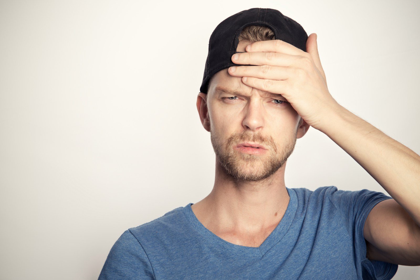 man in blue crew neck shirt covering his face looking confused